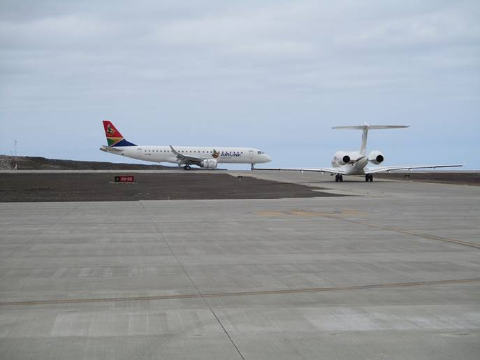 Photo of a Global Express aircraft waiting to taxi onto St Helena Airport's runway as an Airlink E190 lands